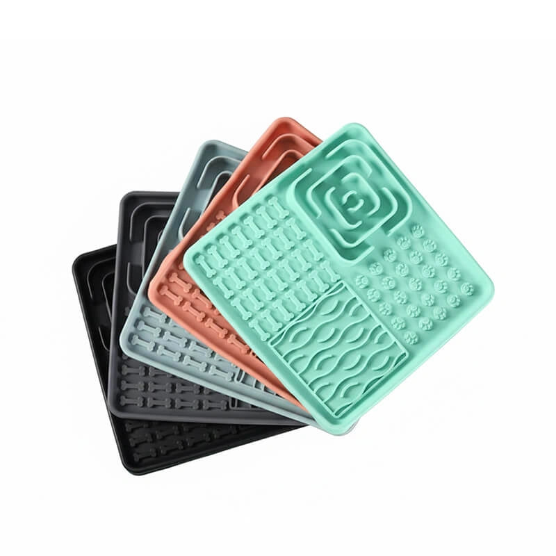 Collection of 3-in-1 enrichment lick mats with suction cups in mint green, grey, orange-red, light blue, and black, showing raised maze and paw print textures for slow feeding.​